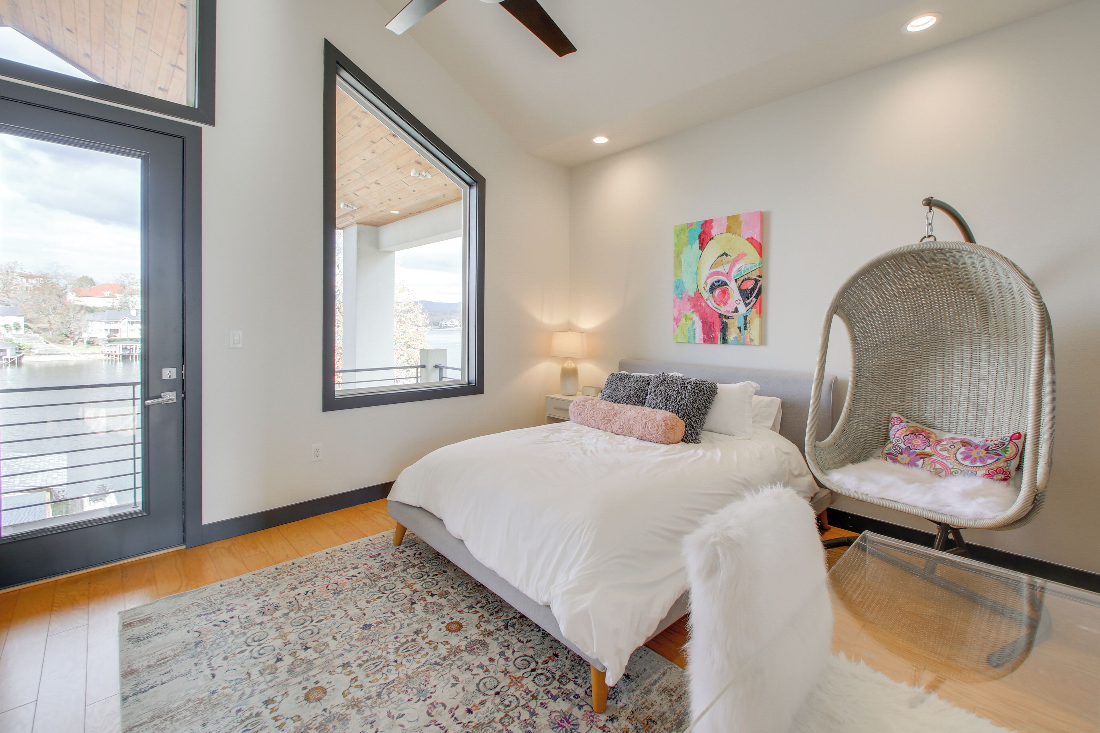 A bedroom with a large bed, a hanging chair, a window, and a painting on the wall.