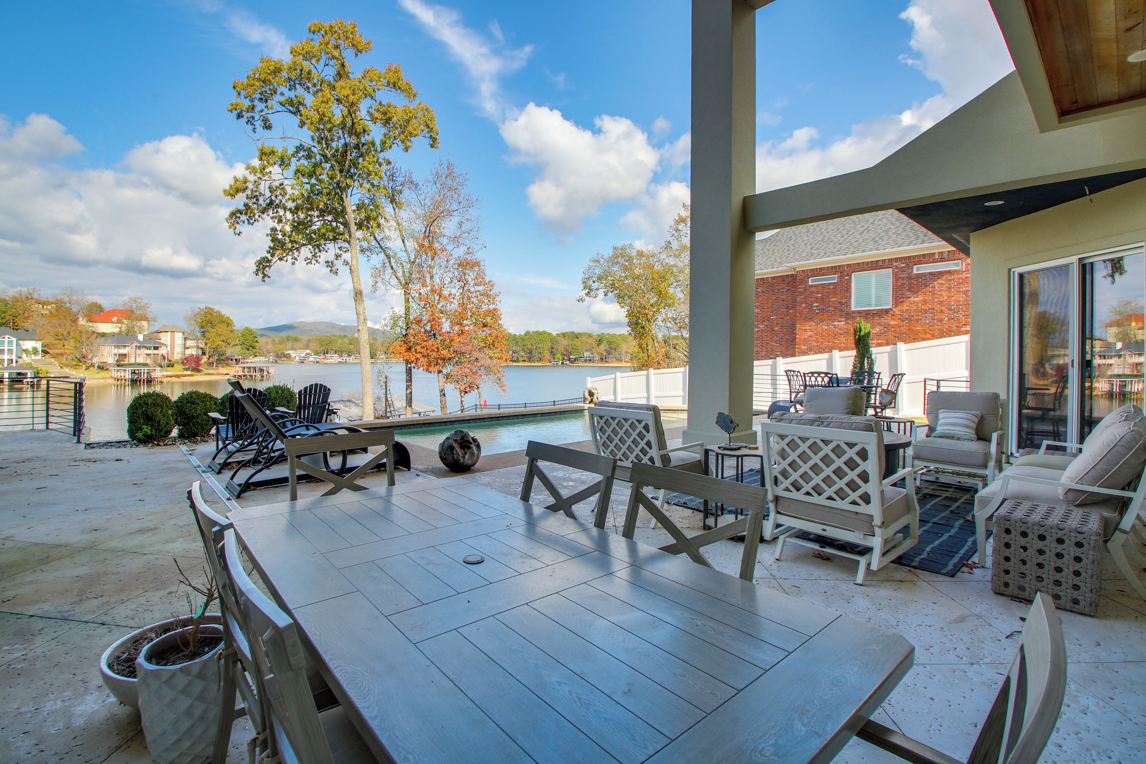 Un patio cubierto con piscina, mobiliario exterior y vistas a un lago y montañas.