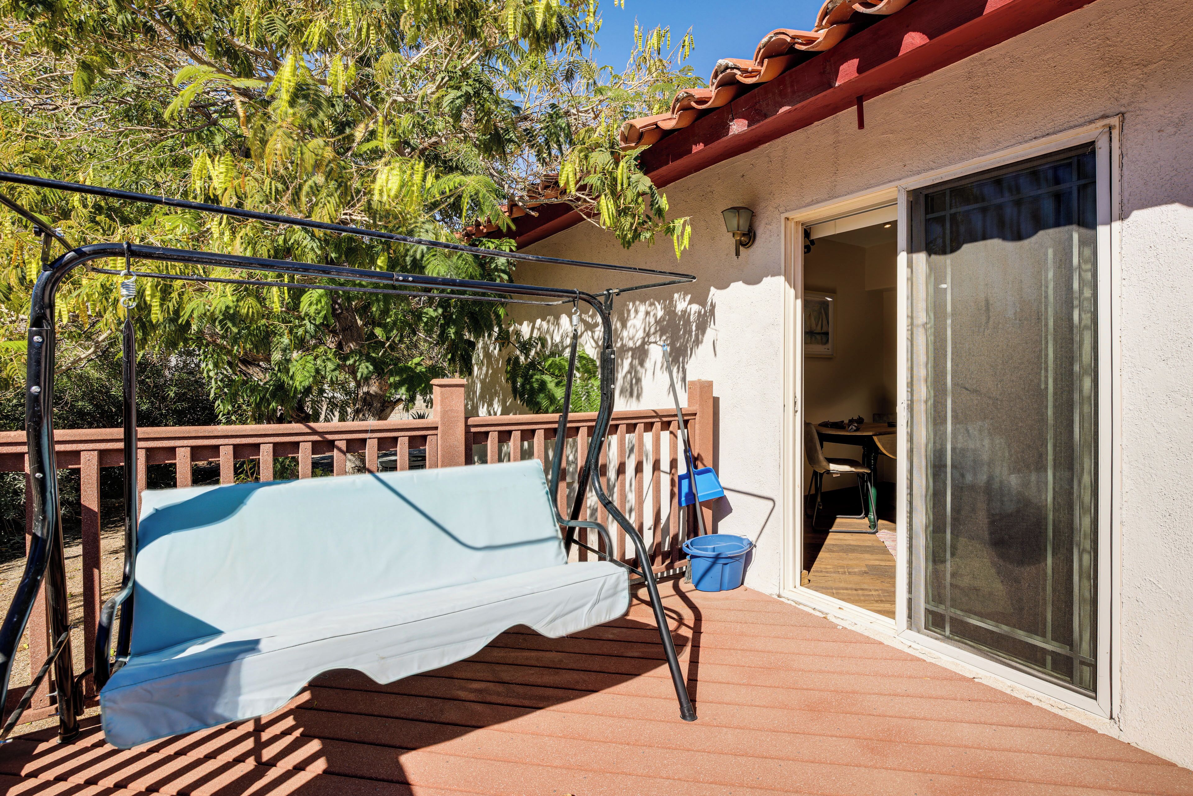 A covered outdoor area with a patio chair, a blue bucket, and a wooden deck.