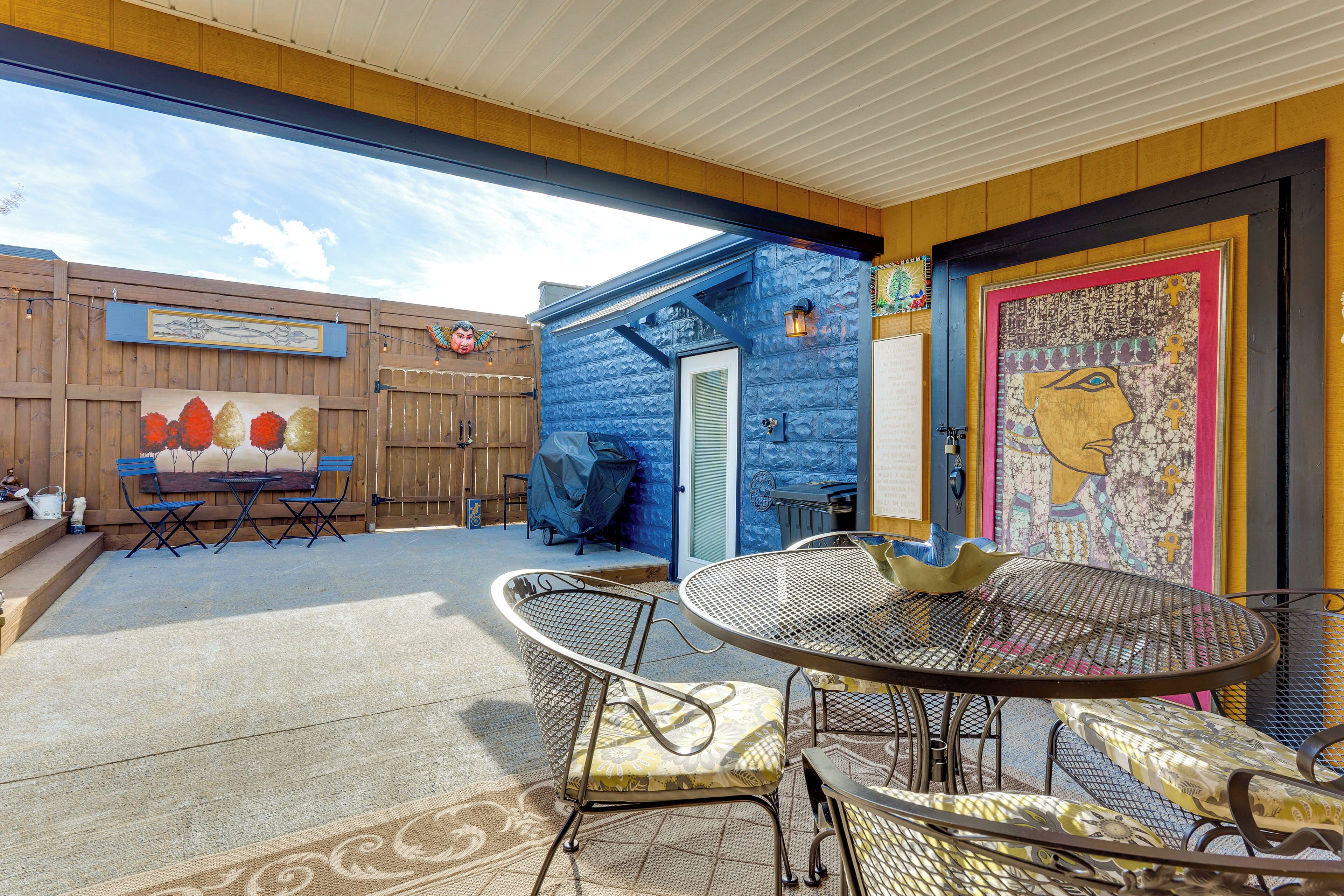 Un patio al aire libre con una pared azul, una mesa redonda de metal y sillas con cojines.