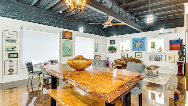 Een ruime kamer met een houten eettafel, stoelen, een plafondventilator en kunst aan de muren.