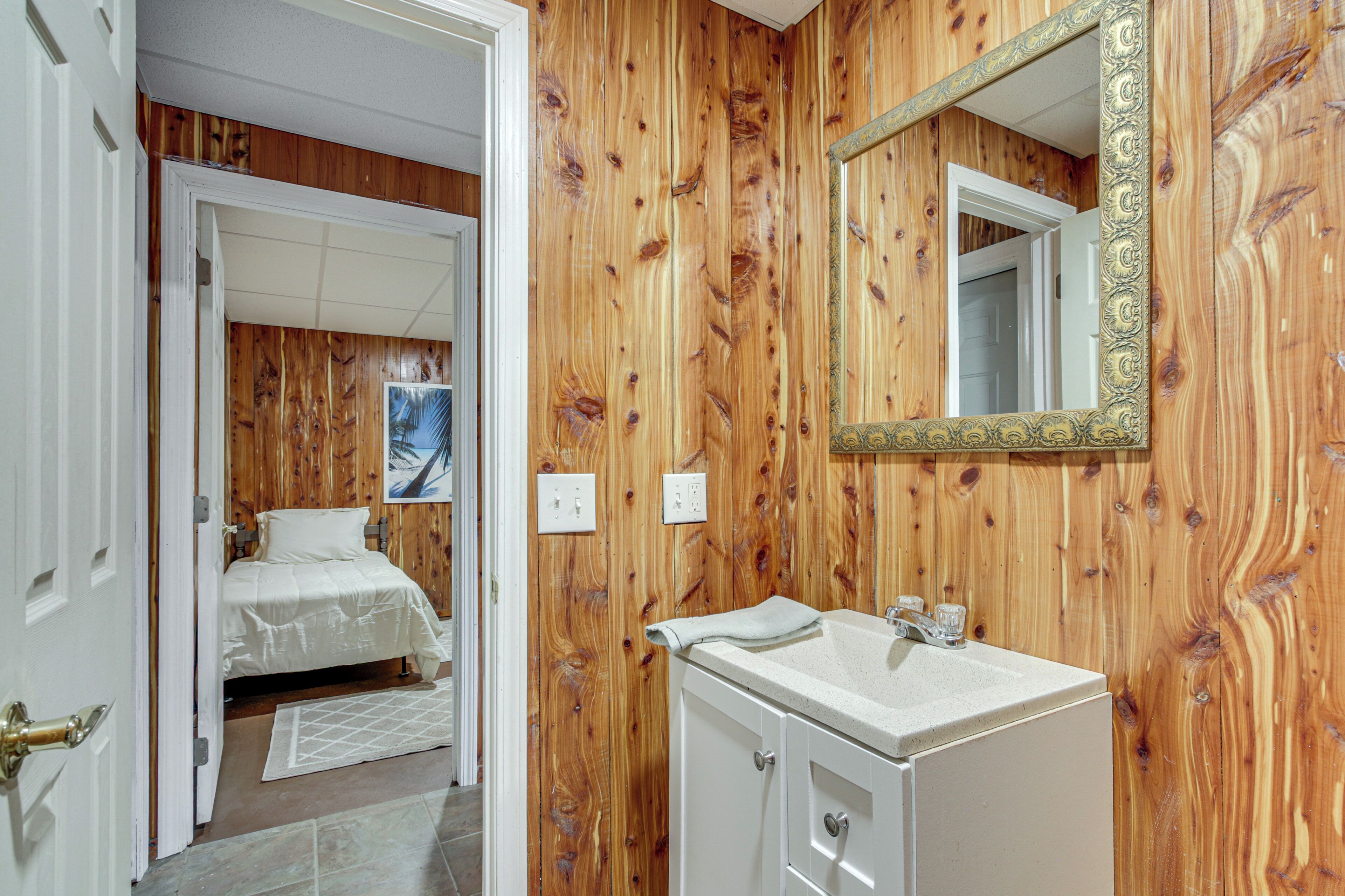 Ein Zimmer mit Holzwänden, einem Bett, einem weißen Waschbecken und einem Spiegel mit aufwendiger Rahmung.