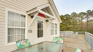 A wooden deck with a glass table and chairs, a covered area with a red roof, and a view of trees. - Near Tennessee River! Pet-friendly Family Cottage! (Savannah)