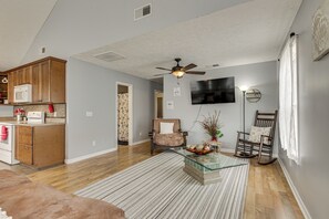 A modern living room with a glass coffee table, a ceiling fan, and a flat-screen TV mounted on the wall. - Near Tennessee River! Pet-friendly Family Cottage! (Savannah)