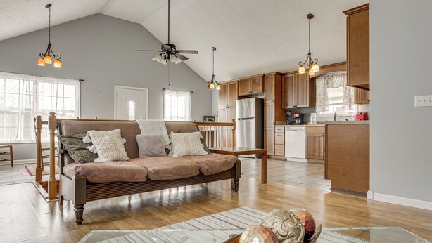 A spacious living room with a large sofa, wooden flooring, and a dining area with a kitchen in the background. - Near Tennessee River! Pet-friendly Family Cottage! (Savannah)