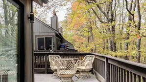A wooden deck with wicker chairs and a table, overlooking a forested area. - Ski-in/ski-out Camelback Mtn Retreat w/ Hot Tub (Tannersville)