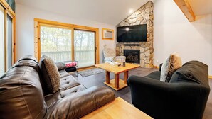 A modern living room with a stone fireplace, leather sofas, and a large TV mounted on the wall. - Ski-in/ski-out Camelback Mtn Retreat w/ Hot Tub (Tannersville)
