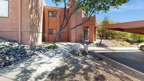 A modern building with a stucco exterior, a tree in the foreground, and a parking area. - 1 BR Condo in Tucson, Mountain Views (Tucson)