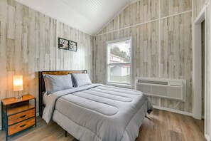 Une chambre avec un lambris en bois, un lit avec une tête de lit, une table de chevet avec une lampe et une fenêtre avec des stores.