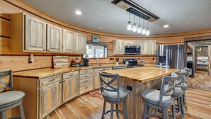Una cocina moderna con armarios de madera, una isla central con taburetes de bar, electrodomésticos de acero inoxidable e iluminación colgante.