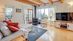 A cozy living room with a sofa, a television, a fireplace, and a large window with curtains. - Pacific View Home: Hot Tub & Ocean/valley Views! (Langlois)