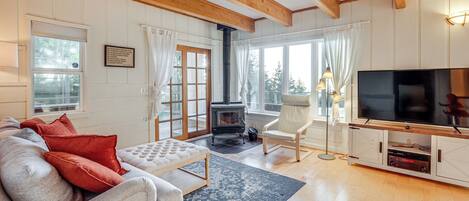 Un salon confortable avec un canapé, un téléviseur, une cheminée et une grande fenêtre agrémentée de rideaux.