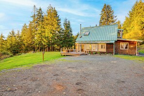 A cabin with a metal roof, wooden exterior, and a deck. - Pacific View Home: Hot Tub & Ocean/valley Views! (Langlois)