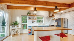 A modern kitchen with a central island, wooden beams, white tiled walls, and a large window. - Pacific View Home: Hot Tub & Ocean/valley Views! (Langlois)