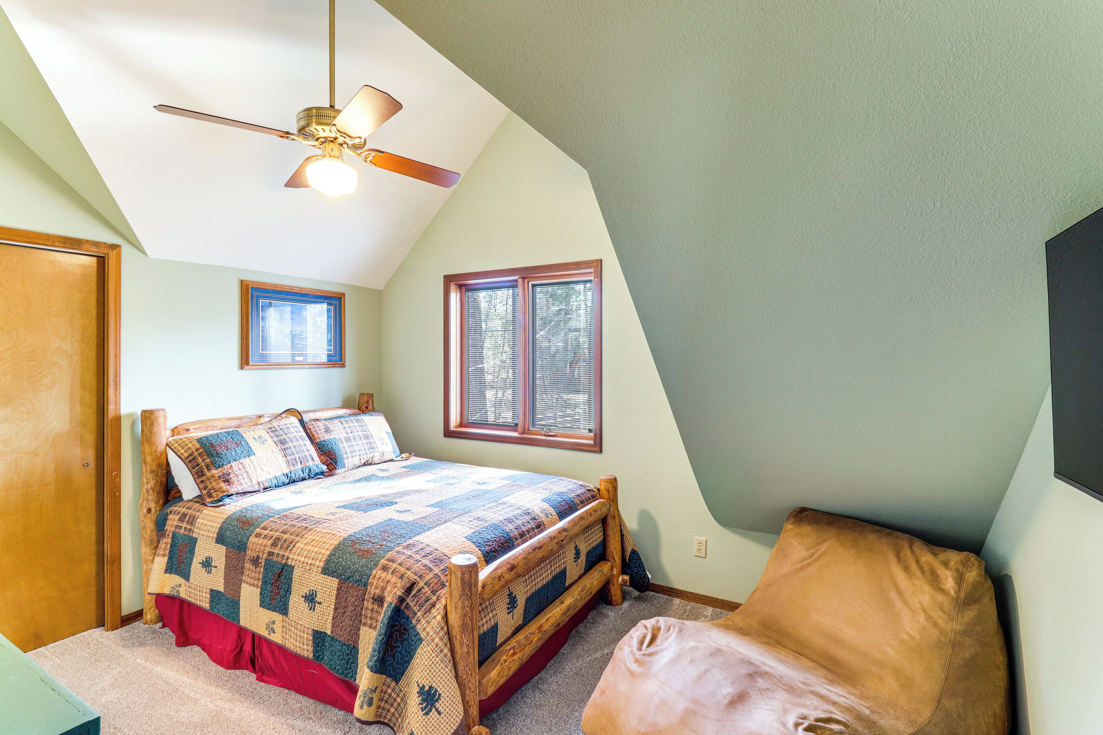 Une chambre avec un lit en bois, un ventilateur de plafond, une fenêtre et une porte.
