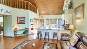 A spacious living area with a wooden ceiling, a leather sofa, a coffee table, and a kitchen area with a bar counter. - Golf, Hike, Explore! Family-friendly Pinetop Haven (Pinetop)