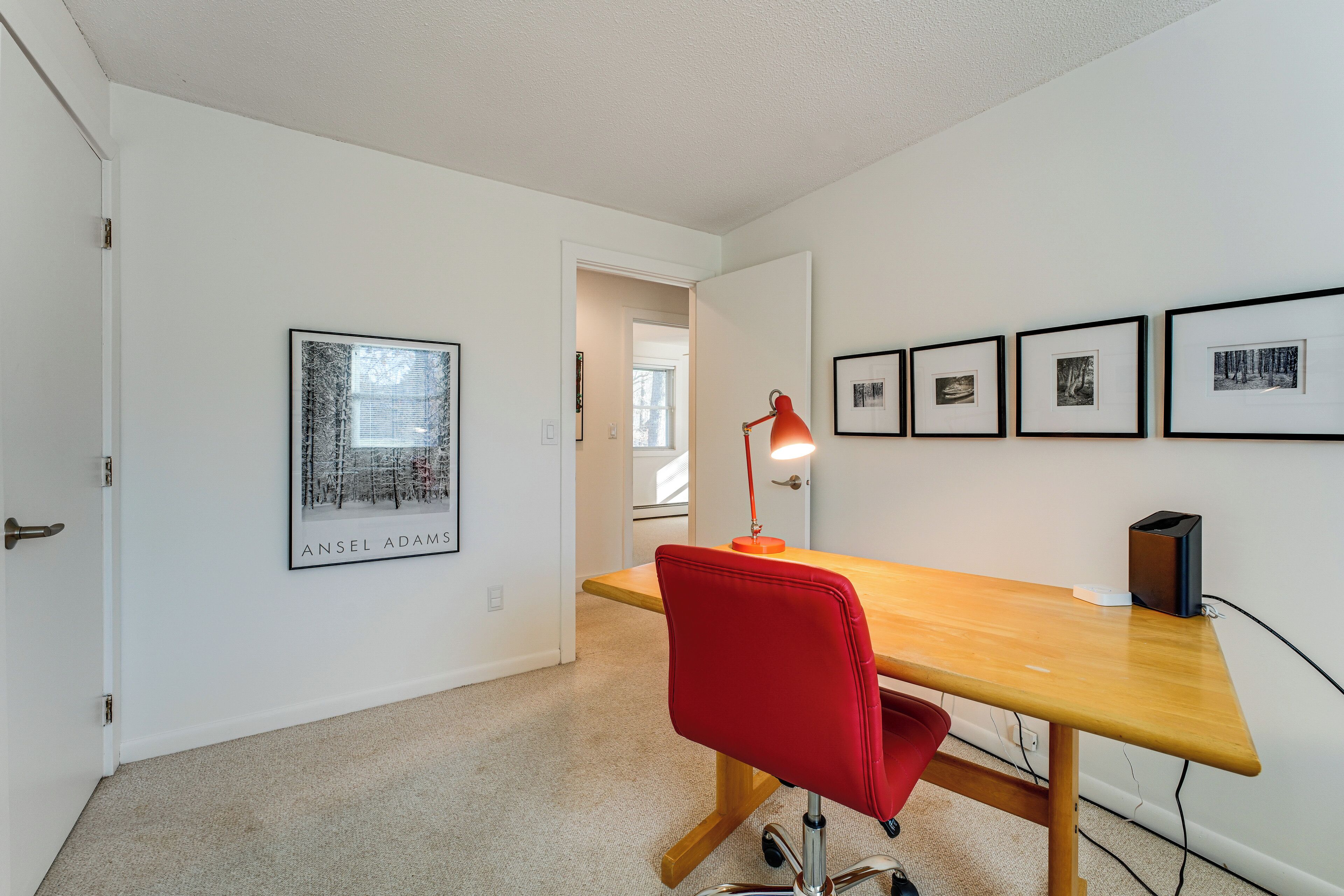 A room with a wooden desk, a red chair, a lamp, and framed pictures on the wall.