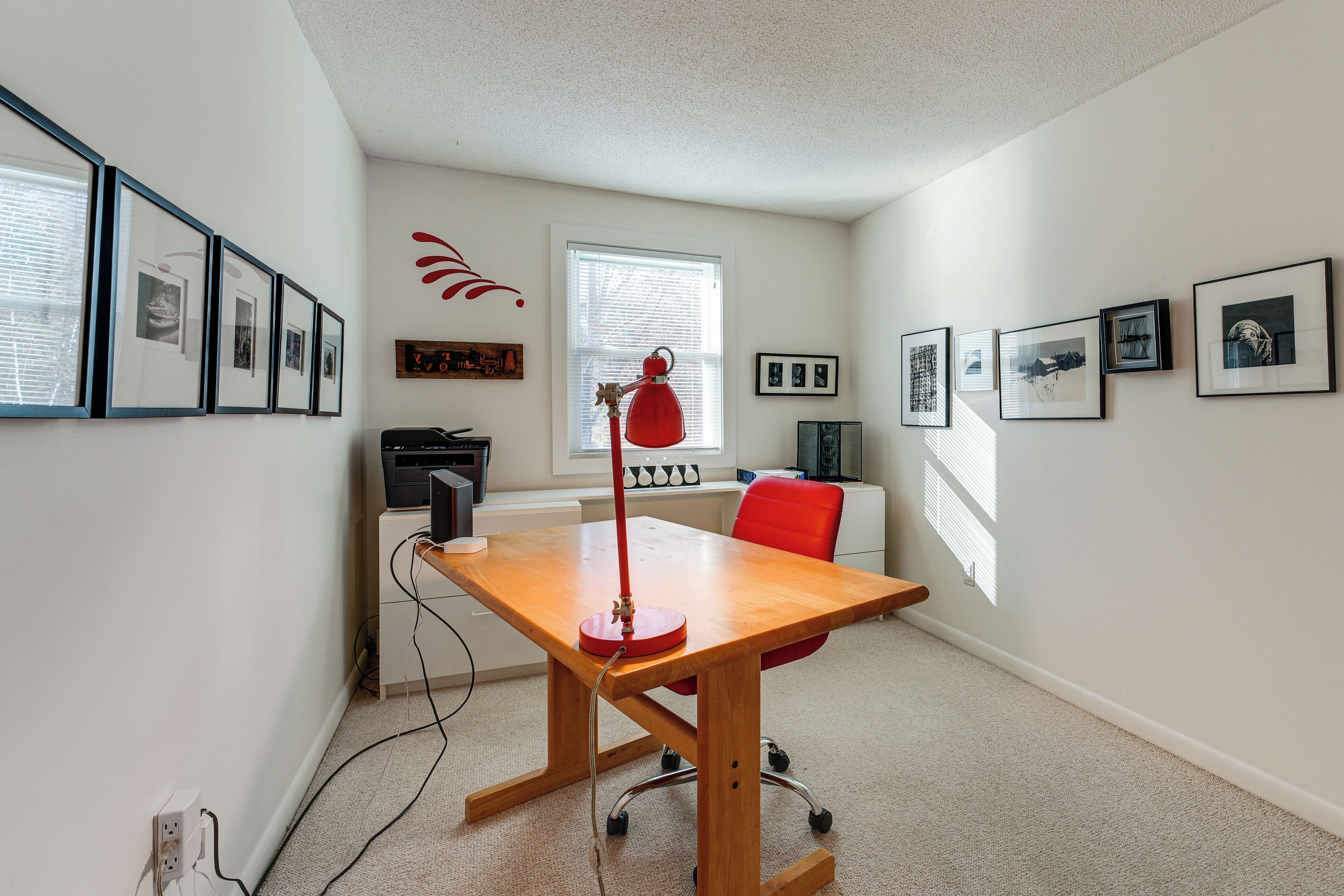A modern office space with a wooden desk, red chair, and framed pictures on the walls.