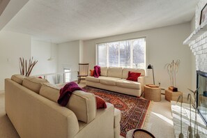A modern living room with a beige sofa, a patterned rug, and a large window providing natural light. - 1 Mi to Maine Street! Mcm-style Home in Brunswick (Brunswick)