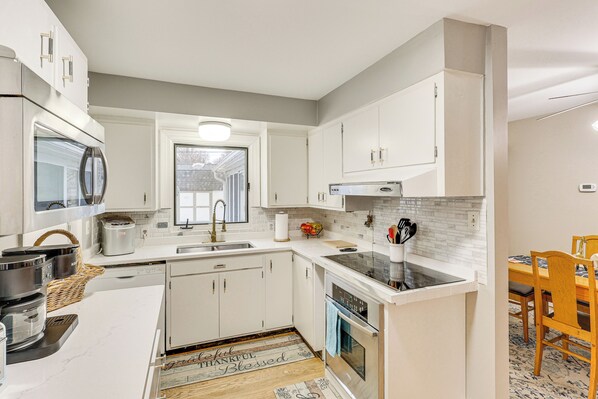 A modern kitchen with white cabinetry, a stainless steel refrigerator, a built-in oven, and a dining area with wooden chairs. - 6 Mi to Dtwn: Cozy Omaha Apt w/ Private Yard! (Omaha)