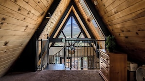 A wooden interior with a sloped ceiling, a staircase, and a view through large windows.