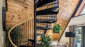 A spiral staircase with black railings, a grey sofa, and a potted plant in a room with wooden walls and a sloped ceiling.