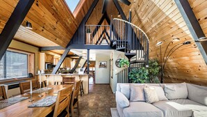 A wooden interior with a dining area, a sofa, and a staircase.
