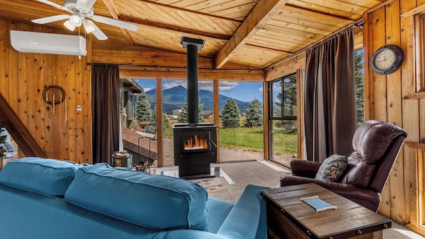 A cozy cabin interior with a blue sofa, leather chair, and a wood-burning stove.