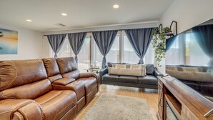A modern living room with leather sofas, a flat-screen TV, and large windows with curtains.
