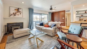 A modern living room with a fireplace, a sofa, a glass coffee table, and a dining area with a chair and a small table. - 1 Mi to CU Boulder! Walkable Condo w/ Indoor Pool (Boulder)