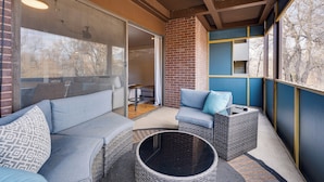 A covered patio with wicker furniture, a glass door leading to an indoor area, and a view of trees through the window. - 1 Mi to CU Boulder! Walkable Condo w/ Indoor Pool (Boulder)