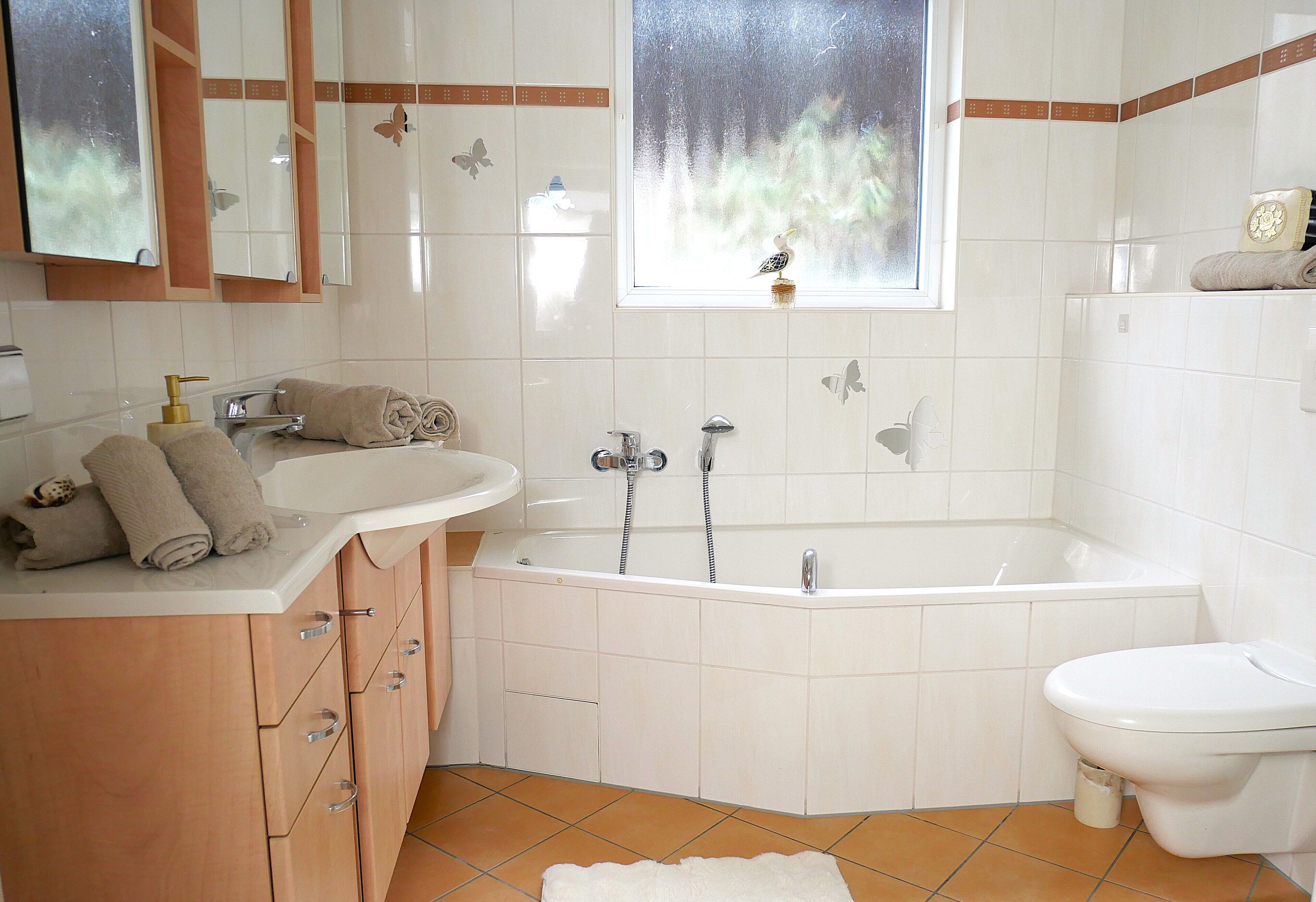 Une salle de bain équipée d’une baignoire, de toilettes, d’un lavabo et d’une fenêtre donnant sur la forêt.
