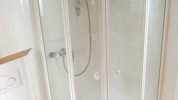 Une cabine de douche fermée par des parois en verre, équipée d’un pommeau de douche à main et d’un flexible de douche à main.