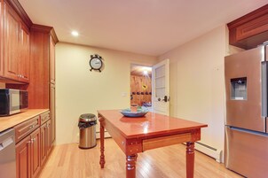 A kitchen with wooden cabinets, a stainless steel refrigerator, a microwave, and a wooden table with a bowl on it.