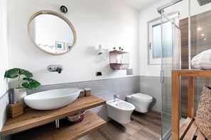 Une salle de bain moderne avec un grand lavabo ovale, un bidet, une douche à parois de verre et un meuble-lavabo en bois.