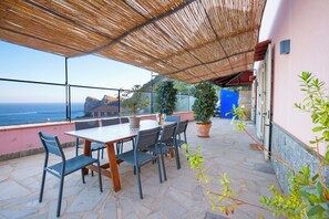 Une terrasse avec une table et des chaises, des plantes en pot et une vue sur la mer.
