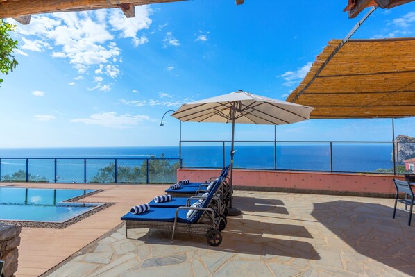 Un espace aménagé au bord de la piscine, avec des chaises longues et un parasol, offrant une vue imprenable sur l’océan.