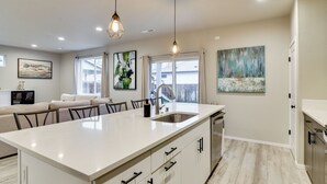 A modern kitchen with a large island, white cabinetry, and pendant lighting. - Family Friendly! Newly Built North Vancouver Home! (Vancouver)