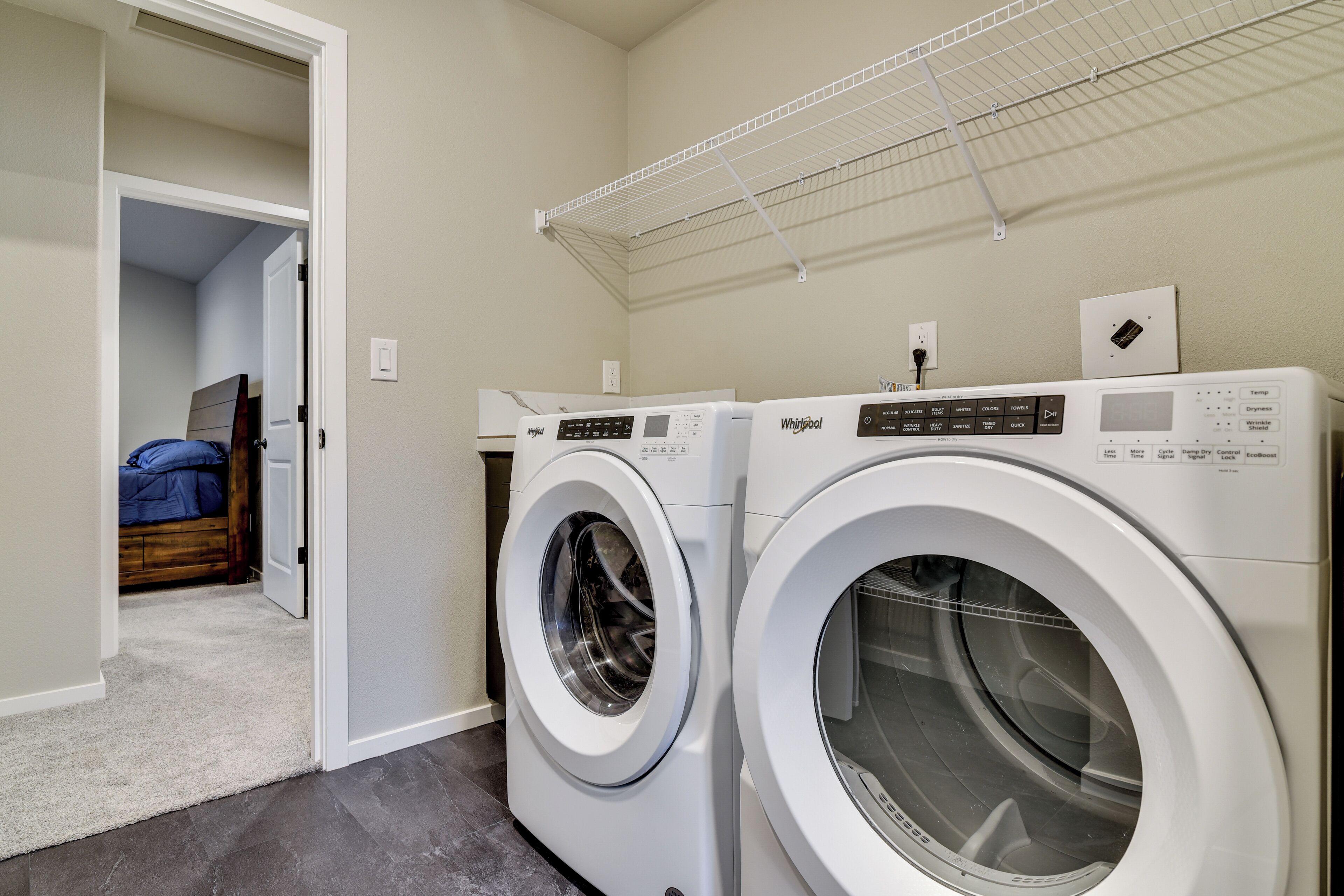 Une buanderie équipée de deux lave-linge et deux sèche-linge à chargement frontal, avec un plafond blanc, et une chambre adjacente.