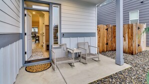 A covered patio area with wicker chairs, a small table, and a wooden fence. - Family Friendly! Newly Built North Vancouver Home! (Vancouver)