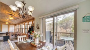 Un coin repas avec une table en bois dressée pour quatre personnes, un lustre et une vue sur l’extérieur grâce à de grandes portes-fenêtres coulissantes.