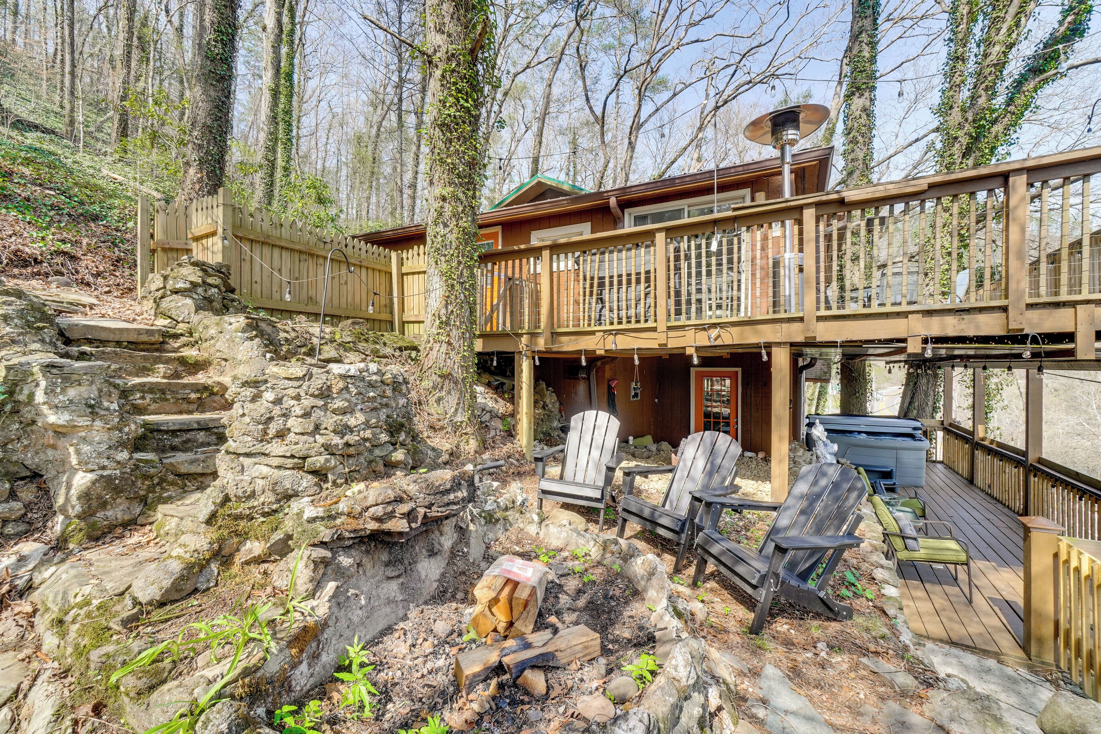 A cabin with a stone foundation, wooden deck, outdoor seating, and a hot tub.