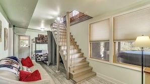 Un escalier menant à une chambre à coucher située en mezzanine, un canapé avec des coussins rouges et une lampe près d’une fenêtre.