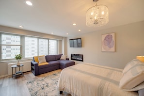 A modern bedroom with a large bed, a sofa, a TV, and a chandelier. - Cozy 12th-floor Studio w/ Lake Erie Views! (Lakewood)