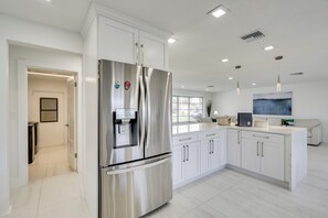 Una cucina moderna con mobili bianchi, elettrodomestici in acciaio inossidabile e illuminazione a sospensione.
