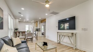 Un salon moderne avec un canapé en cuir, une table basse en verre et un téléviseur posé sur un meuble blanc.