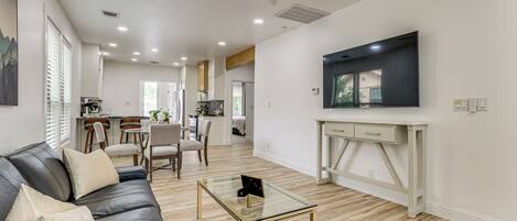 A modern living room with a leather sofa, a glass coffee table, and a TV on a white stand.
