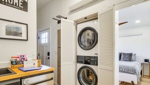 A compact laundry room with a front-loading washer and dryer, a small sink, and a wooden counter with a basket and a blue folder. - Brand New Scandinavian Cabin 5 Mi to Main St Breck (Breckenridge)