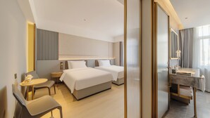 Une chambre d’hôtel moderne équipée de deux lits, d’un bureau, d’une chaise et d’une salle de bain avec un miroir et un meuble-lavabo.