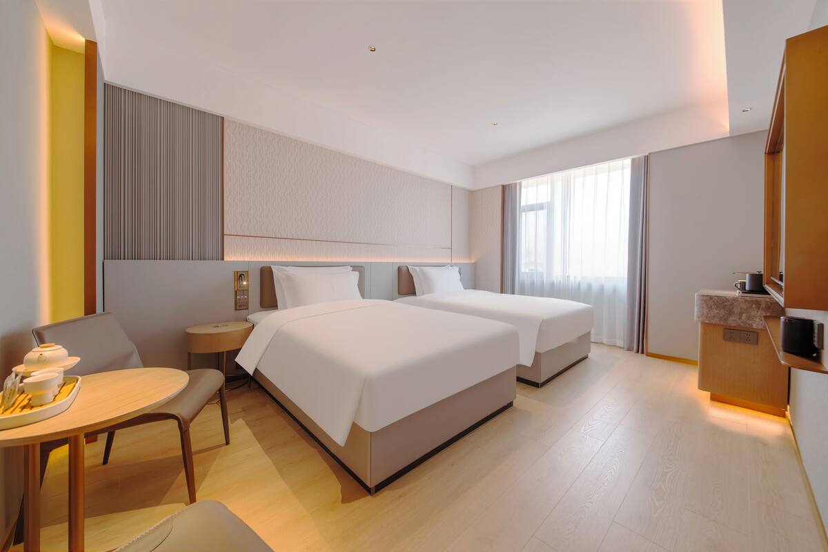 A hotel room with two beds, a small dining table, a bedside table, and a kitchenette area.
